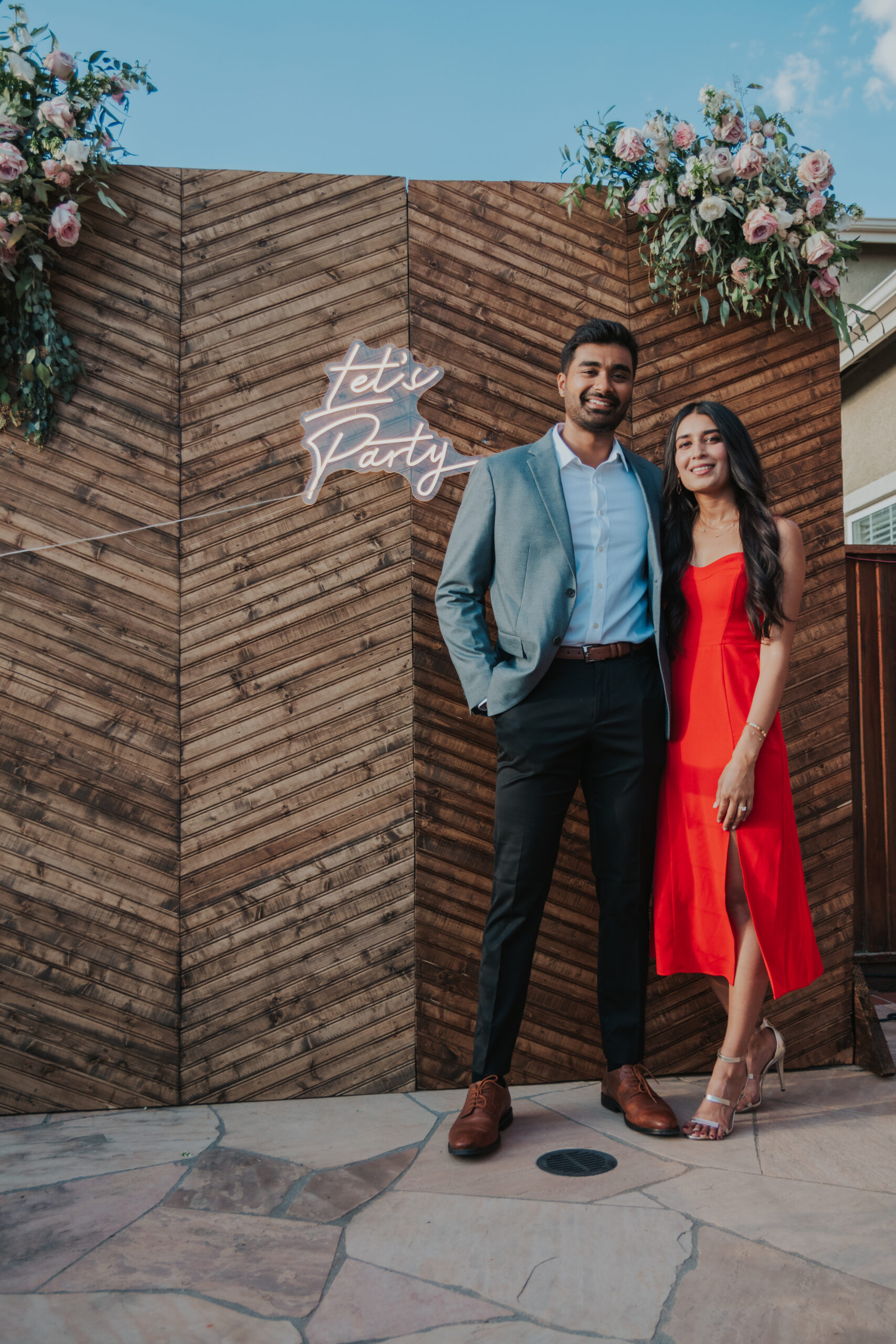 Engaged couple poses in front of wood back drop that says Let's Party.